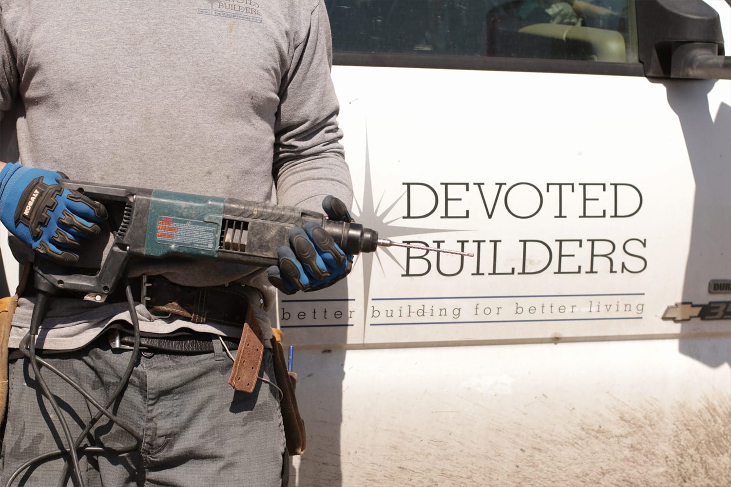 Builder holding a power drill near company vehicle.