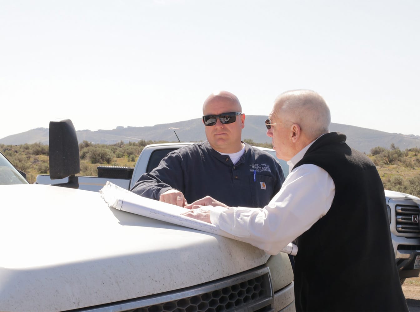 Men discussing plans on vehicle hood outdoors